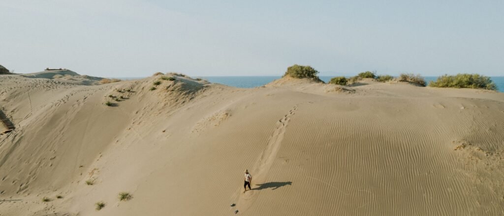 pexels-photo-17304100-17304100 A lone traveler walks on desert sand dunes under clear blue sky.